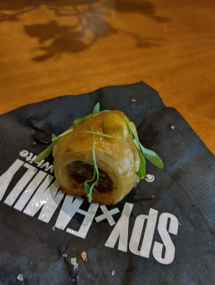 Sausage roll with crispy puff pastry, served with micro-cilantro and a dollop of spicy mustard.